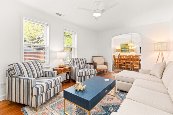 A living room with striped sofas, a blue coffee table, and a dining area with wooden chairs and a painting.