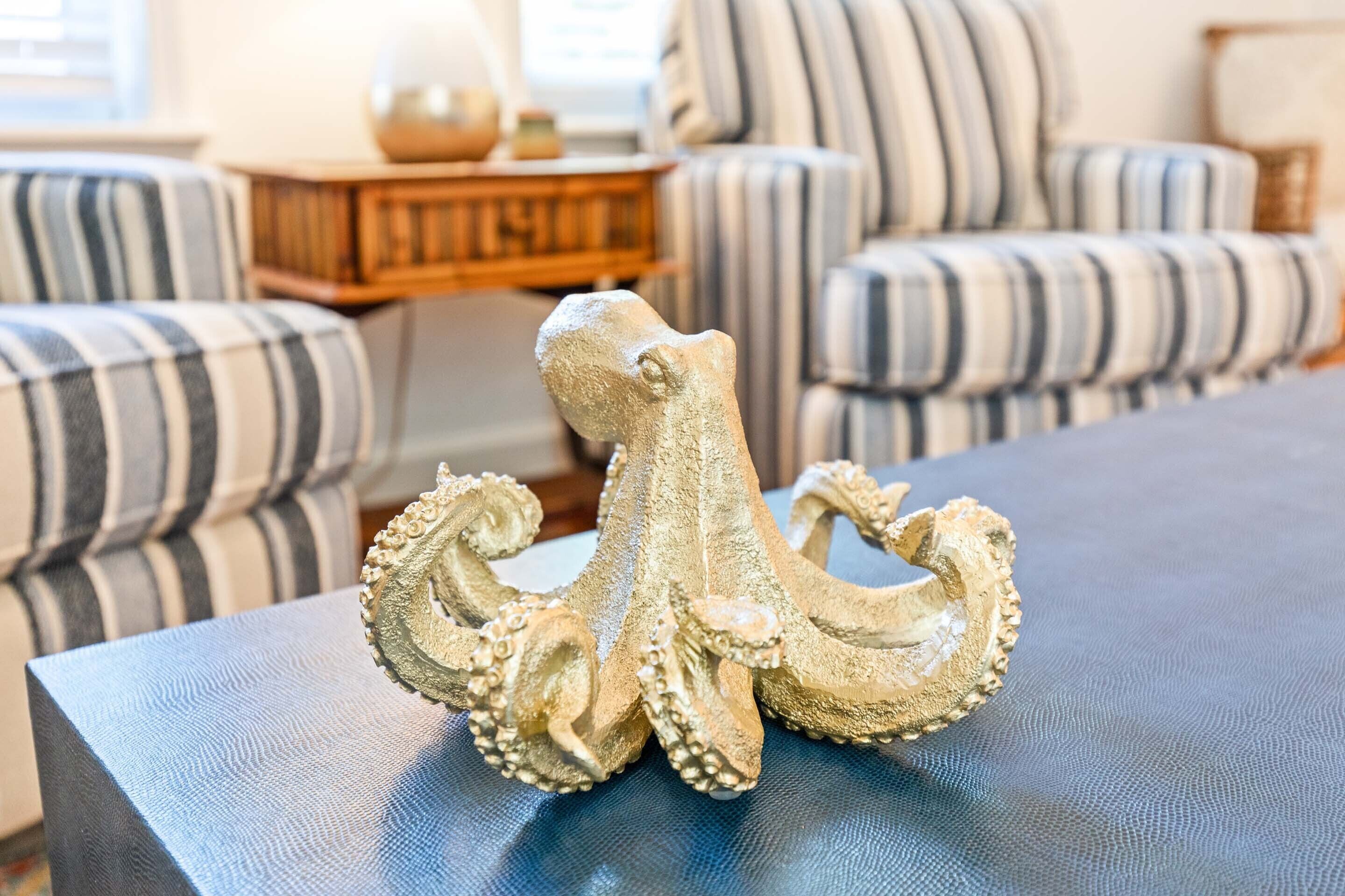 Une sculpture décorative représentant une pieuvre, posée sur une table bleue dans un salon où se trouvent des canapés à rayures.