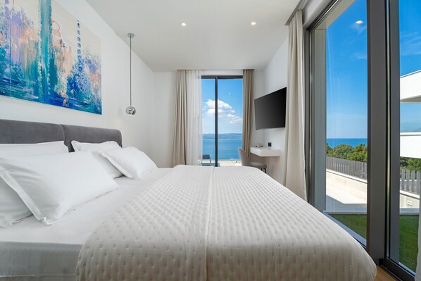 A modern hotel room with a large bed, a flat-screen TV, and a balcony with a view of the sea.