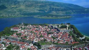 Vista aérea de uma cidade histórica com um castelo fortificado, rodeada por um lago e montanhas.