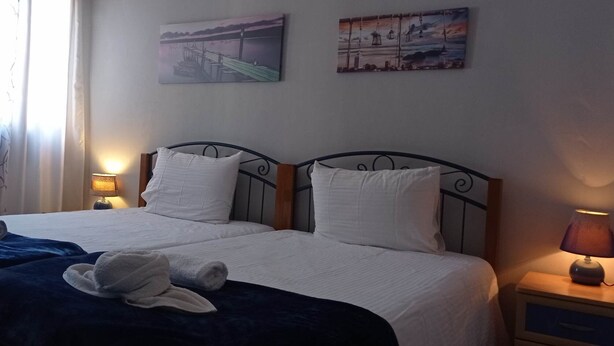 Quarto de hotel com duas camas, cada uma com roupa de cama e almofadas brancas, cabeceira de madeira e mesa de cabeceira com abajur.