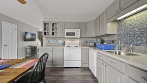 A modern kitchen with white cabinetry, a microwave, a stove, and a sink. There is a dining area with a wooden table and chairs.