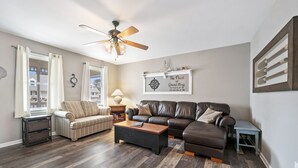 A living room with a dark wood floor, a striped armchair, a leather sofa, a coffee table, and a ceiling fan.