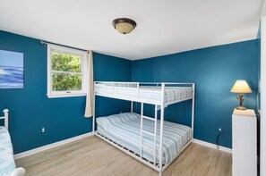 Une chambre avec un lit superposé, une fenêtre donnant sur un paysage verdoyant, une lampe et un tableau au mur.