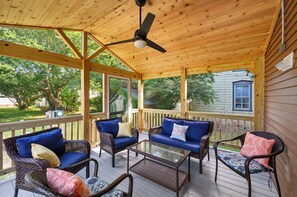 A covered porch with wicker furniture, a ceiling fan, and a view of the surrounding greenery. - The Mane Escape by Seaside Vacations & Sales (Chincoteague Island)