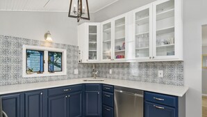 Una cucina con mobili di colore blu scuro, pensili bianchi, una lavastoviglie in acciaio inossidabile e una finestra con vista sugli alberi.