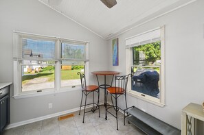Une cuisine avec deux fenêtres, une table à manger avec des chaises, et une vue sur le jardin arrière.
