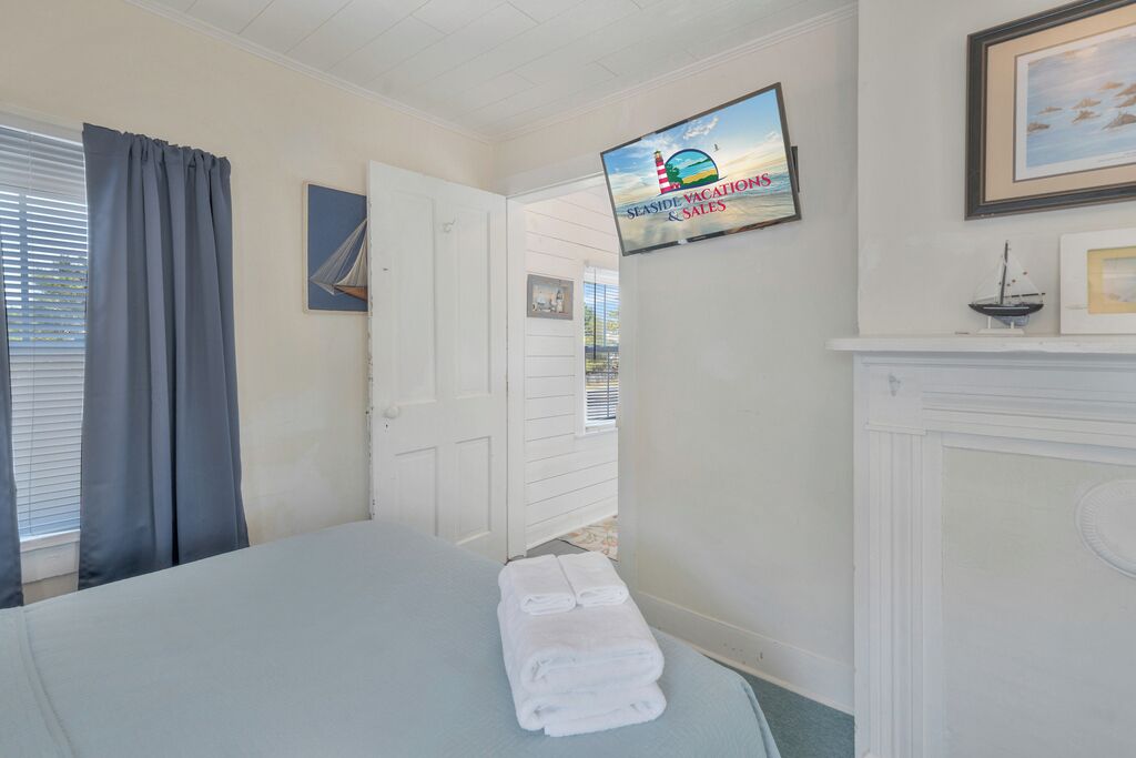 Une chambre d’hôtel avec un lit, un téléviseur fixé au mur, une cheminée et une vue sur la plage, accessible par une porte ouverte.