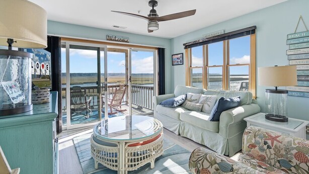 A spacious living room with a glass table, a sofa, and a view of the beach. - Wonderview 208 by Seaside Vacations & Sales (Chincoteague Island)
