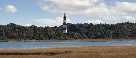 Un faro junto a una masa de agua, con un bosque en el fondo.