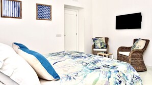 A bedroom with a bed, two wicker chairs, a TV, and an air conditioning unit. - Tyrrhenian Sea View Apartment (Campania)