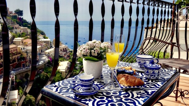 A balcony with a table set for breakfast, overlooking a coastal town. - Tyrrhenian Sea View Apartment (Campania)