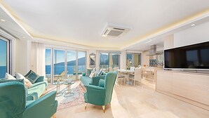 Un soggiorno moderno con una grande TV, divani color acquamarina e vista sul mare.