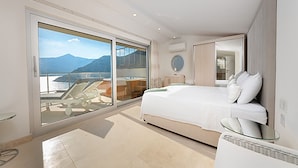 Una moderna camera d'albergo con un ampio letto, un balcone vista mare e montagne, e un piccolo angolo salotto.