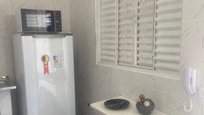 Una cucina compatta con frigorifero, microonde e una finestra con persiane.