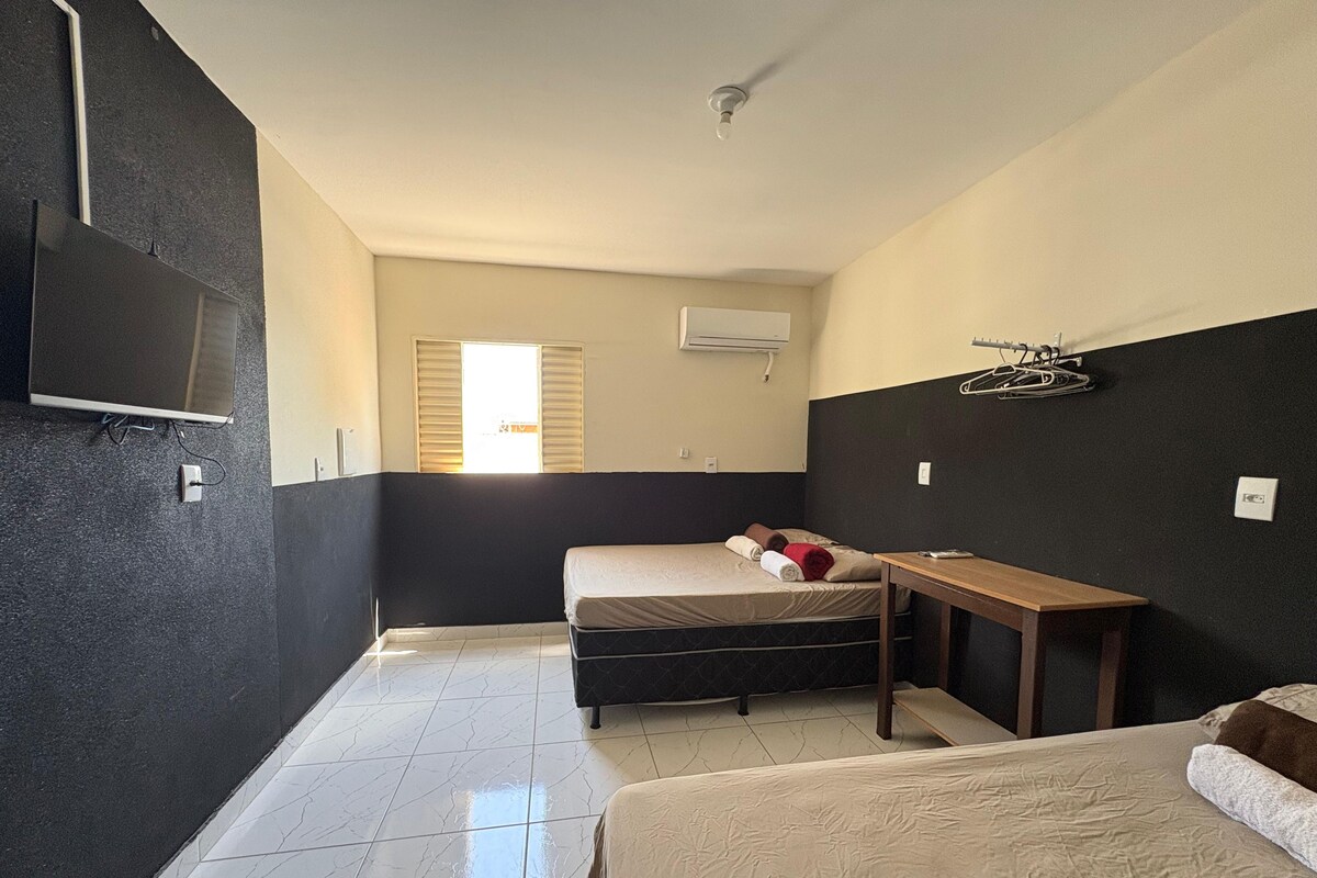 Una habitación de hotel con una cama, una mesita, un televisor montado en la pared y una ventana con persianas.