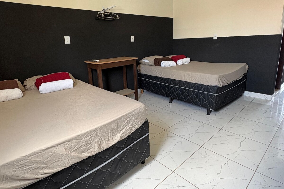 Habitación de hotel con dos camas, una mesita y una lámpara fijada a la pared.