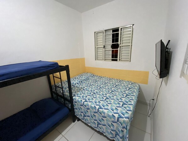Un alojamiento pequeño con una sola habitación, una cama litera, una ventana con contraventanas y un televisor fijado a la pared.