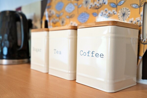 Tres contenedores blancos con tapas de madera etiquetados como 'Sugar', 'Tea' y 'Coffee'.