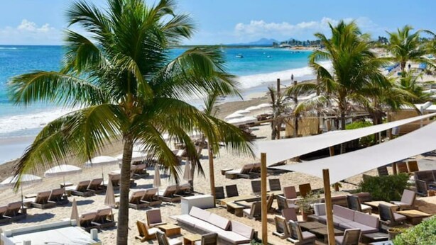 Um resort à beira-mar com espreguiçadeiras e guarda-sóis, uma praia arenosa e vista para o oceano.