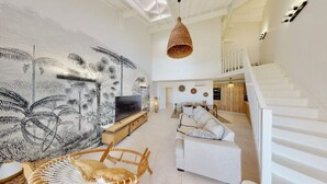 Uma sala de estar ampla com teto alto, um grande mural na parede, um sofá branco, uma mesa de jantar e uma escada.