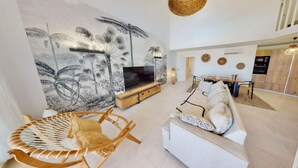Uma sala de estar moderna com um grande mural na parede, um sofá, uma TV e uma poltrona de vime.