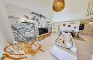 Un salon moderne avec une grande fresque murale, un canapé, un téléviseur et un fauteuil en osier.