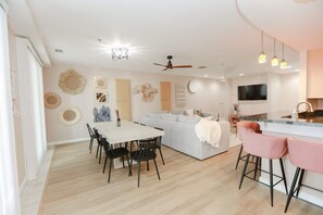 A modern kitchen with a built-in oven, a dining area with a white table and black chairs, and a grey sofa with a white throw blanket.