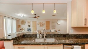 A kitchen with granite countertops, a double sink, a ceiling fan, and pendant lighting. - Sojourn Sanctuary Seaside Escape (Virginia Beach)