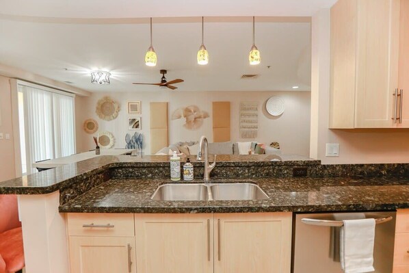 A kitchen with granite countertops, a double sink, a ceiling fan, and pendant lighting. - Sojourn Sanctuary Seaside Escape (Virginia Beach)