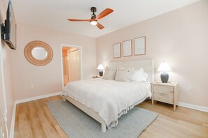 Ein Schlafzimmer mit Bett, Nachttischen, Deckenventilator, Spiegel und gerahmten Bildern an der Wand.