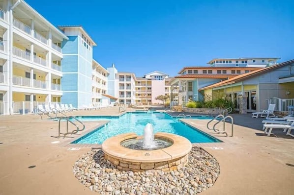 A hotel pool area with a central fountain, lounge chairs, and a multi-story building with balconies. - Sojourn Sanctuary Seaside Escape (Virginia Beach)
