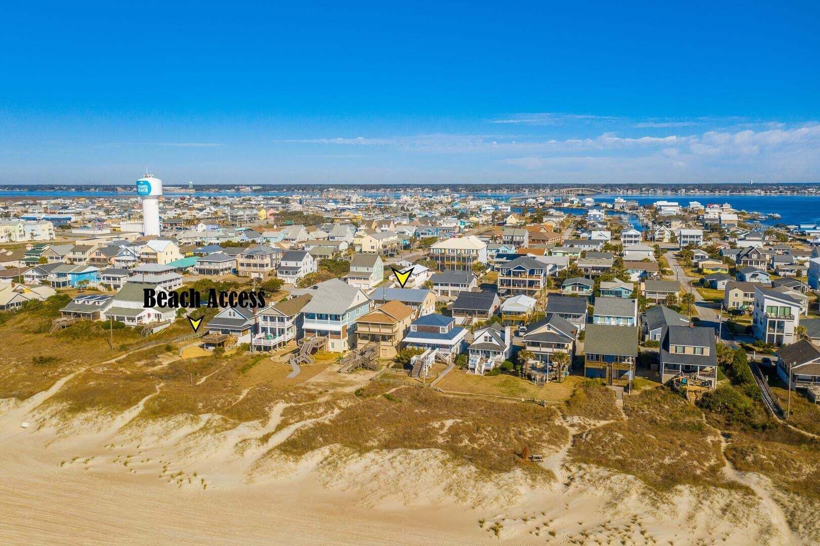 An aerial view of a coastal residential area with houses, a lighthouse, and a beach access path.