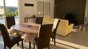 Un coin repas avec une table ronde, des chaises et un canapé. On y trouve également un téléviseur et une fenêtre avec des stores.
