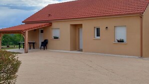 Un bâtiment d’un seul étage, avec un toit recouvert de tuiles rouges, des murs de couleur beige et un patio abrité comprenant une table et des chaises.