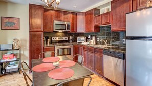 A kitchen with wooden cabinets, stainless steel appliances, and a dining table with placemats. - Beautiful Condo Central to Main Street and Peak 9! (Breckenridge)