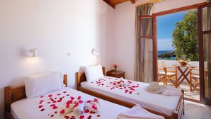 Quarto de hotel com duas camas, varanda com mesa e cadeiras, e vista para o mar.