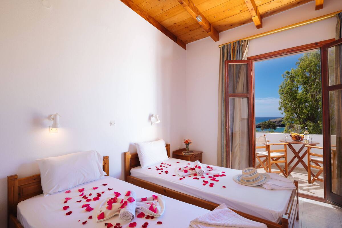 Ein Hotelzimmer mit zwei Betten, einem Balkon mit Tisch und Stühlen und Blick aufs Meer.