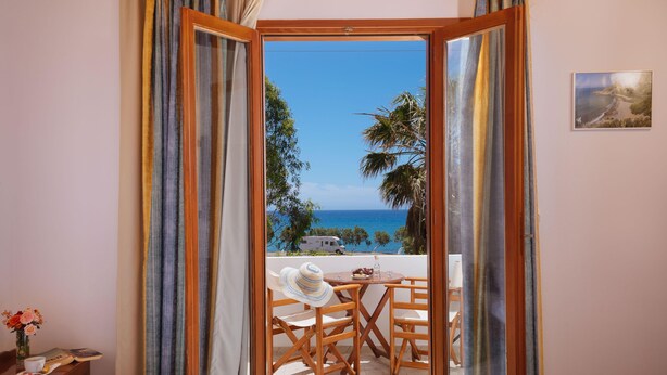 Um quarto com uma cama, uma mesa com cadeira e vista para o mar.