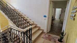 Una escalera con barandilla geométrica, una puerta con letrero azul y una planta en maceta.