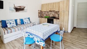 Un espacio habitable compacto con una mesa de comedor, sillas, un sofá con cojines, un ventilador de techo, una zona de cocina y una puerta.