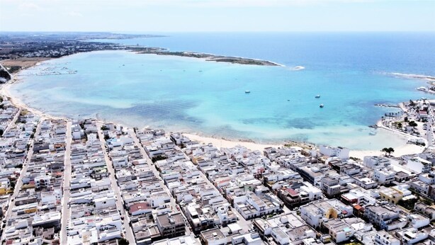 An aerial view of a coastal town with a dense cluster of buildings near the beach and a marina with boats. - Appartamento lu Sule (Porto cesareo)