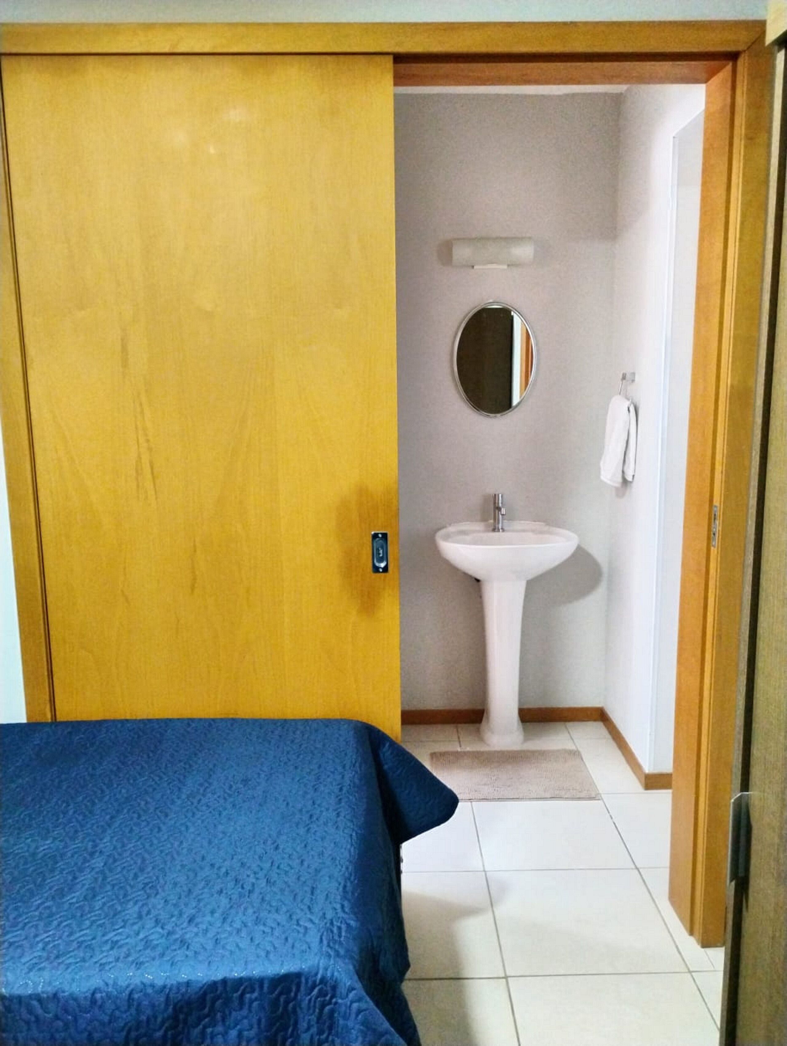A room with a bed, a bathroom with a sink and a mirror, and a door leading to another room.