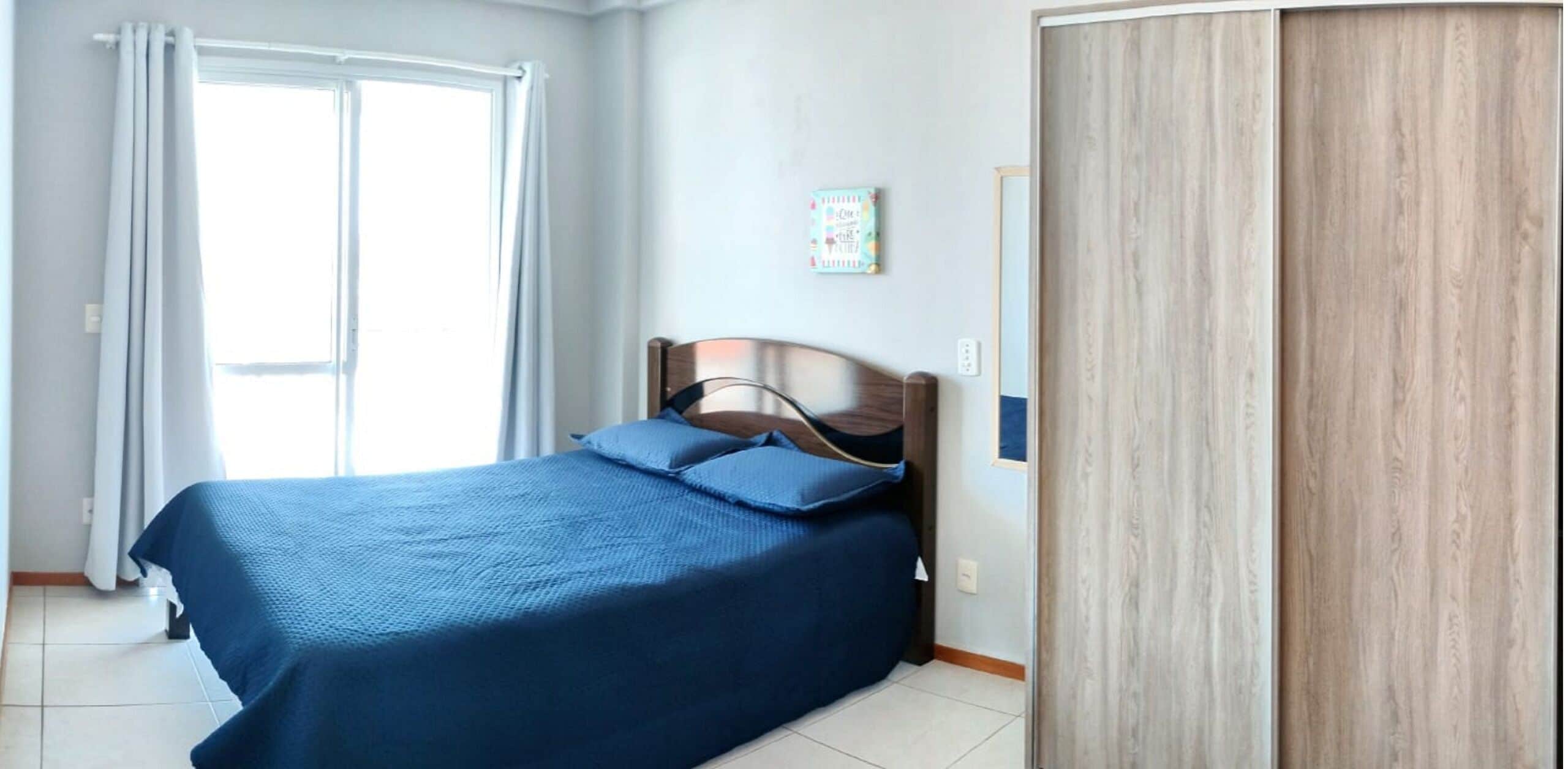 Un dormitorio con cama, ventana con cortinas, armario de madera y un pequeño adorno en la pared.