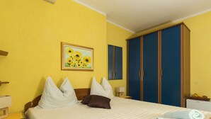 A hotel room with a bed, pillows, a painting of sunflowers, a wardrobe, and a nightstand with a lamp. - Rooms Tupina by Paulina - Standard Double Room With Balcony and Sea View (Zupa dubrovacka)