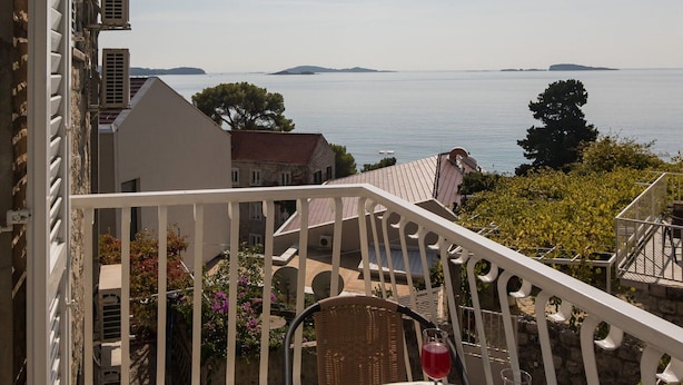 A balcony with a view of the sea, a wicker chair, and a table with two glasses of red drink. - Rooms Tupina by Paulina - Standard Double Room With Balcony and Sea View (Zupa dubrovacka)
