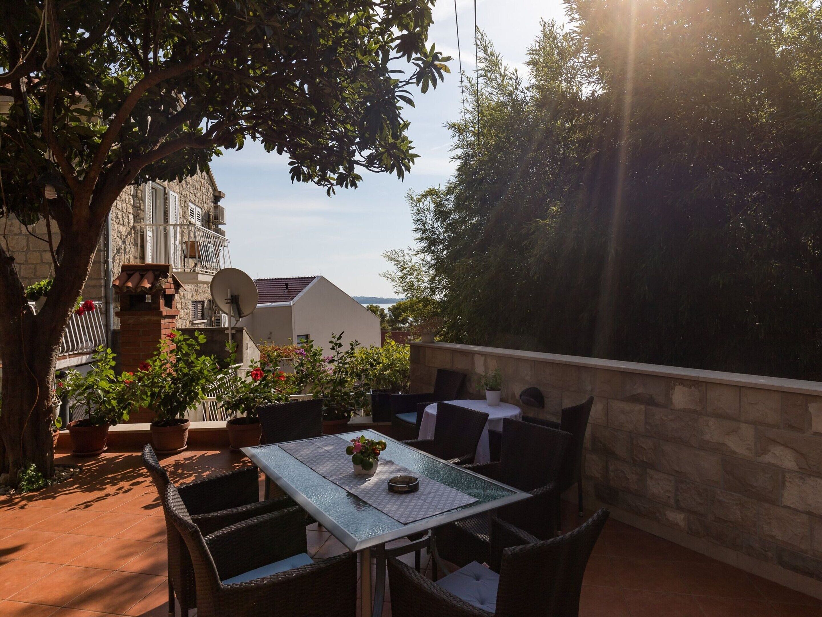 An outdoor patio with a table and chairs, surrounded by potted plants and a stone wall.