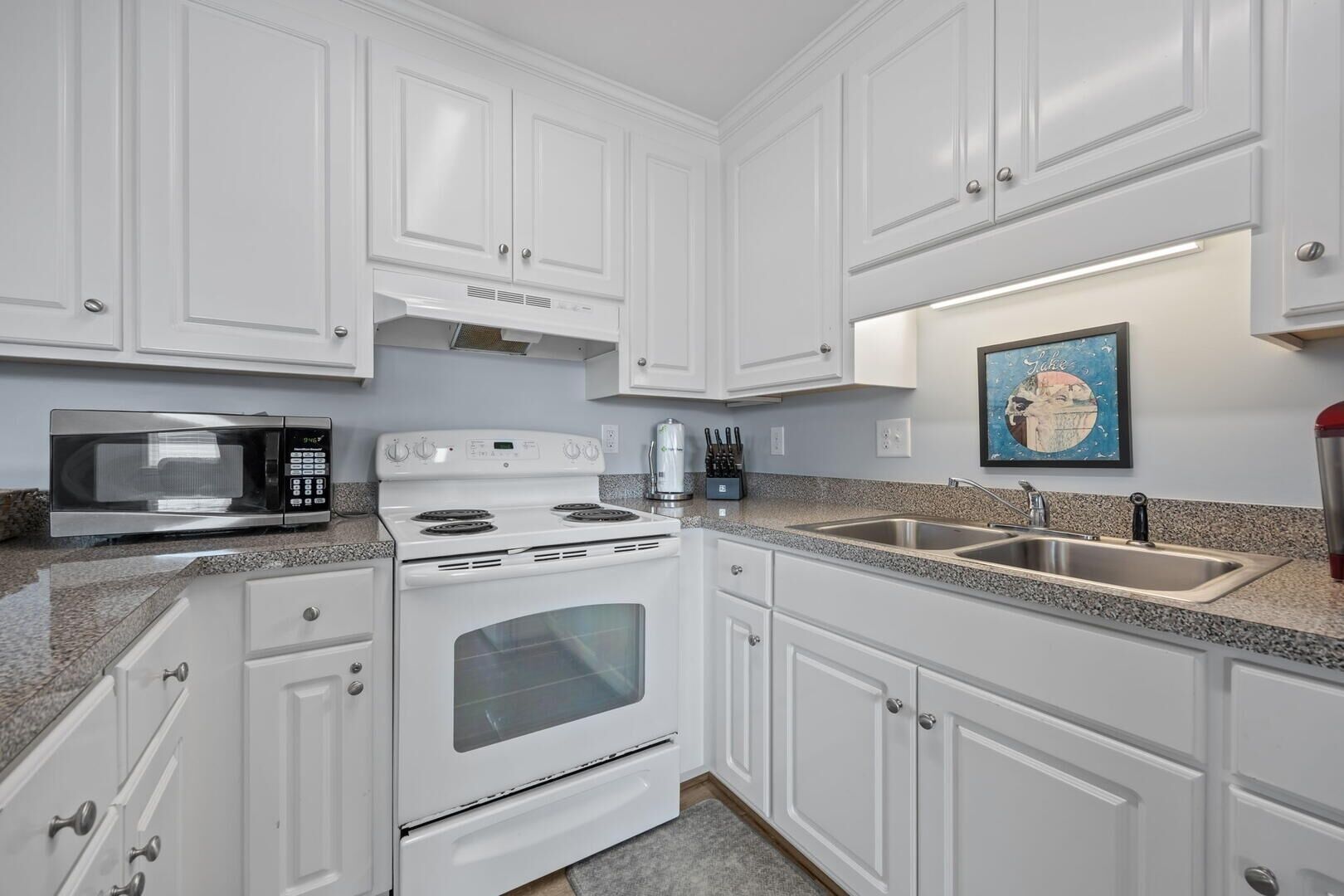 A kitchen with white cabinets, a stainless steel microwave, a stove, and a sink.