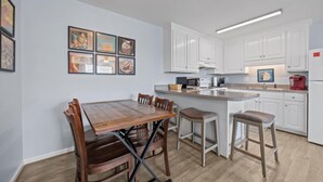 Ett kök med vita skåp, ett matbord i trä och barstolar.