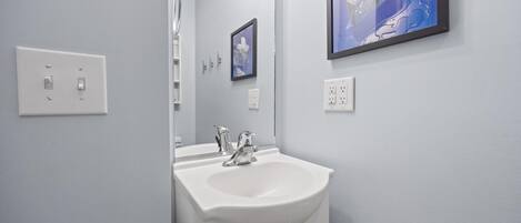A bathroom with a white sink, a mirror, a framed picture on the wall, and a door leading to another room.